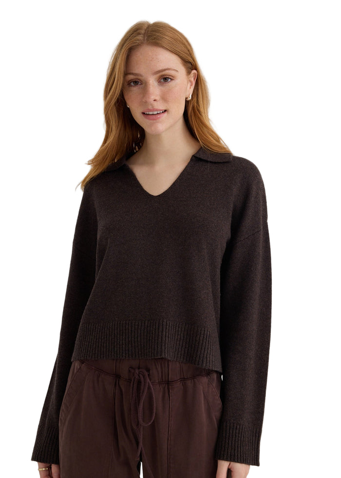 Woman wearing a brown sweater and pants against a plain background