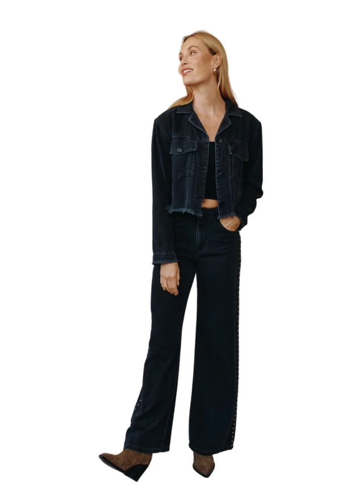 Woman wearing a dark denim jacket and jeans against a plain background
